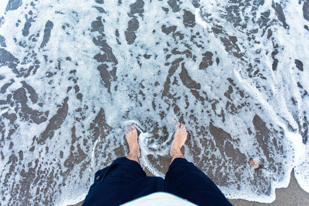 在沙子的蓝色波浪与男性脚