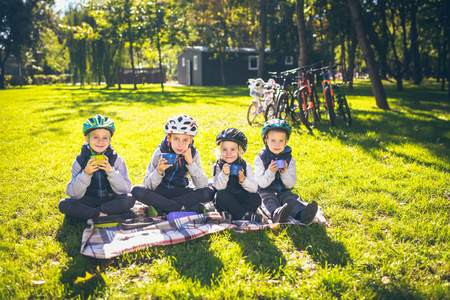 主题活跃家庭节日性质..成群的人，小孩子，三个兄弟姐妹，坐在自行车旁，在公园的绿草草坪上休息，喝杯子和热水瓶茶。