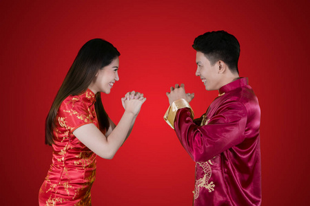 中国年轻夫妇穿旗袍，互相祝贺的形象。 红色背景拍摄