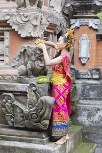 穿着传统服装，在寺庙里的雕刻雕像上放祭品的美丽的巴厘岛女子