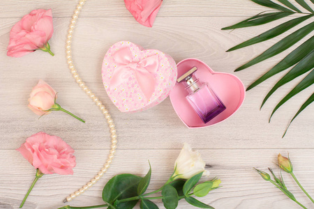 礼品盒心形，瓶香水，粉红色的花和绿叶在木制背景。 上面的风景。 庆祝概念。