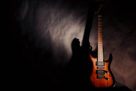 在黑暗的背景上的电吉他。墙上的吉他的影子