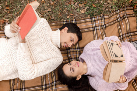 情侣在爱坐在秋天的公园和阅读书籍
