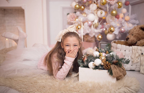 圣诞快乐庆典。 漂亮的小女孩穿着裙子躺在圣诞树附近。 寒假。 新年快乐。