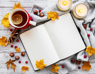 秋天在木制背景上平躺着，有一杯笔记本茶，还有枯黄的落叶