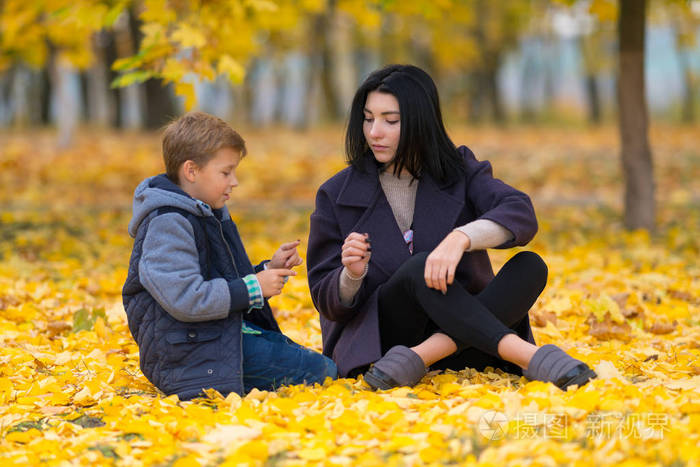 一位母亲和她的儿子在秋天公园的一个场景中坐在黄色的落叶交谈