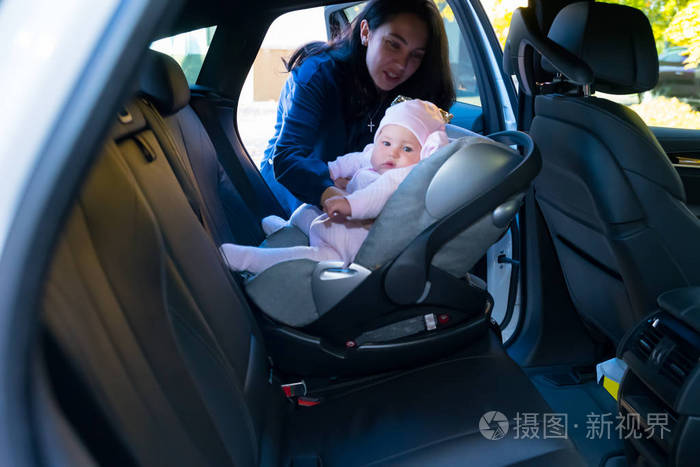 母亲把婴儿放在汽车后座上，从车的另一边看