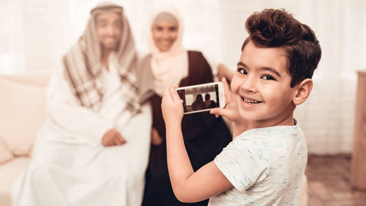 阿拉伯男孩在家拍幸福家庭的照片。 一家人坐在沙发上。 使用数字设备。 微笑的男孩在家。 穆斯林家庭。 微笑的男孩。 年轻的阿拉伯
