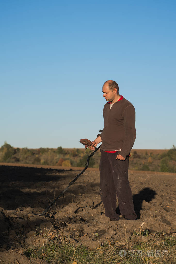 寻宝者手中拿着金属探测器严肃地扫视着土壤