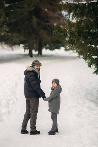 愉快的父亲与他的儿子穿过公园在下雪的冬天天气