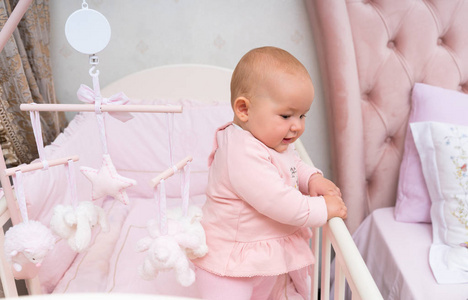 一个快乐的婴儿在粉红色的婴儿床和卧室的场景与悬挂的移动。