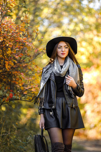 美丽的女人在黑色礼服和帽子在秋天