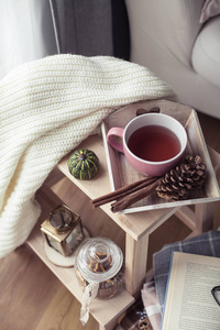 针织温暖毛衣一杯热茶秋天装饰一本书一个南瓜在木椅上。 舒适的秋天装饰。 秋季内部沙发。 跌倒。 冬天。