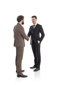 棕色西装胡须年轻商人和他黑色西装英俊同事握手的孤立肖像。 伙伴关系概念