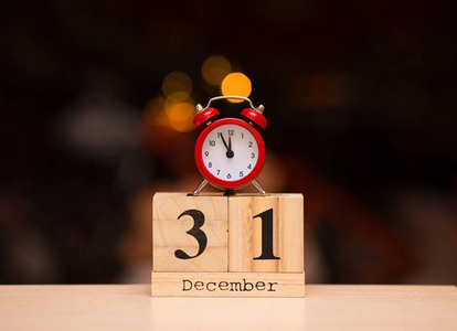 十二月三十一日在木制日历上,红色闹钟在黑暗模糊的背景上.