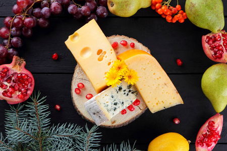 深色木板和圣诞树树枝上的奶酪和水果。 瑞士奶酪Dorblu荷兰奶酪圣诞节。 乳制品柠檬葡萄梨石榴罗旺浆果