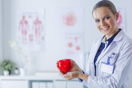 年轻女医生抱着一颗红色的心, 站在医院的背景上