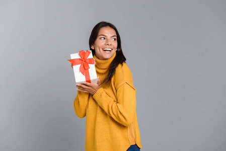 一个快乐兴奋的女人的形象，在灰色的墙壁背景上，抱着盒子，惊喜的礼物。