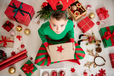 好奇的小男孩穿着圣诞睡衣坐在地板上，打开他的圣诞礼物的顶部。