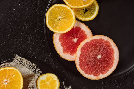 在深色背景的盘子里有各种种类的新鲜柑橘水果