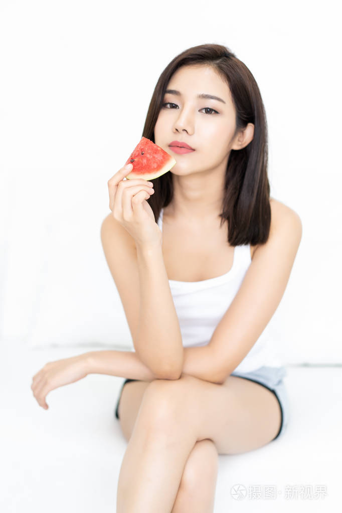 一位美丽的亚洲年轻女子抱着西瓜看着坐在白色沙发上的相机焦点西瓜的