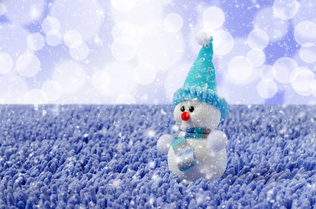 雪人纳塔尔带帽子和围巾的玩具雪人. 下着雪. 蓝色背景照片