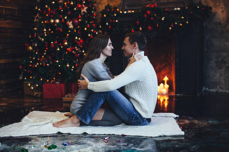 晚上, 浪漫的情侣穿着舒适的毛衣在圣诞树和壁炉附近亲吻