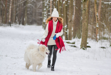 白雪皑皑的冬季森林公园里的漂亮年轻女子在和她的狗一起玩耍时令
