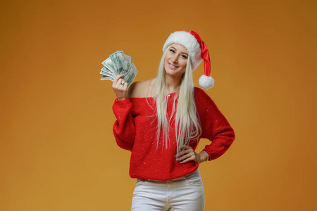 漂亮的白种人年轻快乐的女人戴着红色的圣诞帽，手里拿着礼品盒和黄色背景的。 中了彩票的现金。 新年假期2019概念。