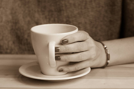 女性手中的白色咖啡杯。 用一杯热饮料温暖你的手。 在咖啡馆见面。 咖啡店里的女孩。 早上在餐厅喝咖啡。 手上手镯上的红线。 红色