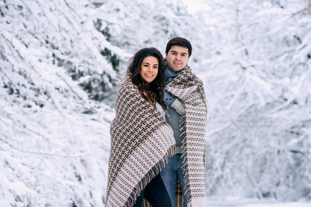 快乐可爱的一对夫妇用温暖的毯子盖着，在一个下雪的公园里散步。 怀孕概念。