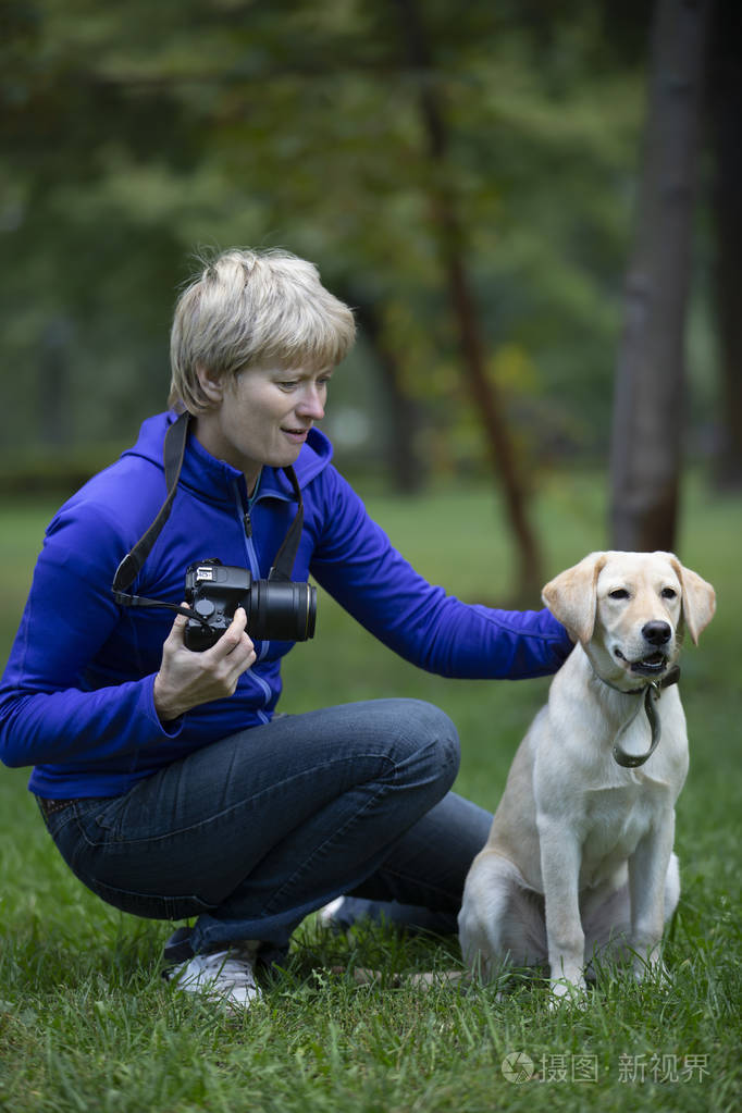 专业摄影师. 一个自信的成年女人手里拿着相机,在公园里给狗拍照