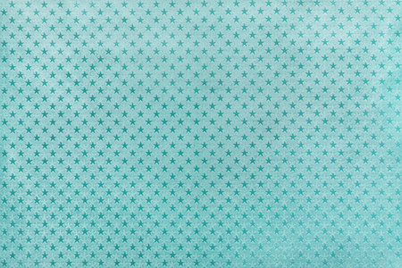 浅蓝色背景从金属箔纸与闪闪发光的星星图案特写。 绿松石金属化包装纸表面的纹理。