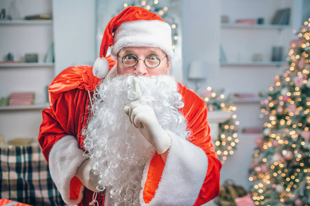 惊呆了的圣诞老人用一只手拿着白胡子, 透过眼镜看着镜头。他肩上有红色的包