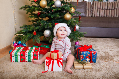愉快可爱的女婴在圣诞老人帽子拿着圣诞礼物在圣诞树在家里