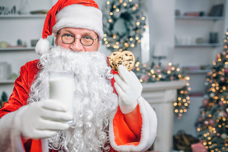 圣诞老人手里拿着一杯牛奶和两个饼干。是他提供的男人看着镜头