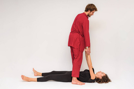 瑜伽姿势的照片在地板上进行两次伸展和在白色背景下放松。 男人在镜头前伸展女人。