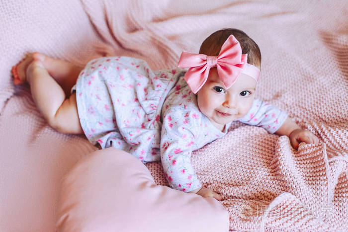 有蝴蝶结的婴儿躺在针织的粉红色毯子上