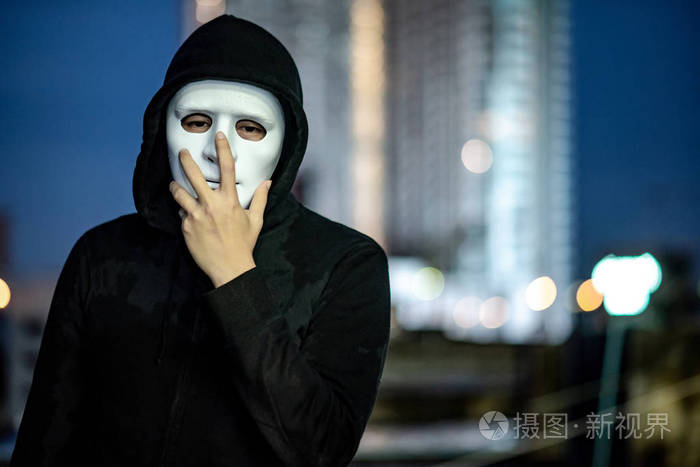 穿白色面具的神秘帽衫人在黄昏的时候站在废弃建筑的屋顶上双相情感