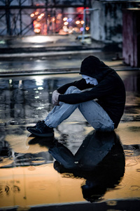 神秘的帽衫男人在白色面具下拥抱着他的膝盖,坐在废弃建筑的屋顶上的