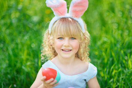 可爱的有趣女孩，在花园里有复活节彩蛋和兔子耳朵。 复活节的概念。 复活节猎蛋的笑孩子。 孩子在公园里，篮子里装满了鸡蛋，春天的概