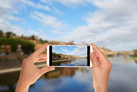 一位游客正在用手机拍摄意大利佛罗伦萨的阿尔诺河码头和维乔桥的照片