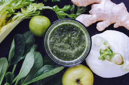 排毒健康绿色冰沙在一个玻璃黑色背景与配料菠菜芹菜，姜茴香，石灰和苹果。 饮食健康，清洁，吃素食的概念。 上面的风景。