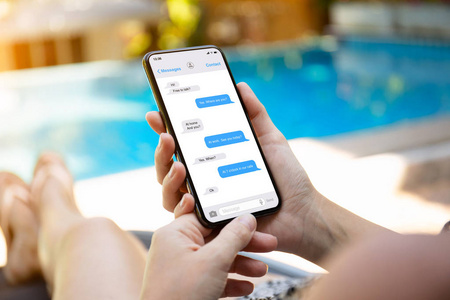在游泳池旁的女人拿着手机，屏幕上有应用信使