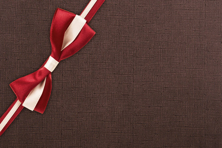 红色和白色礼品丝带和结上棕色纹理图案背景。 礼品盒包装概念