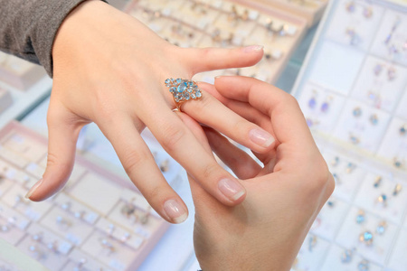 珠宝店里的一个女孩试着用手指在商店橱窗的背景上戴着钻石的金戒指。 女珠宝商。 买东西和购物。