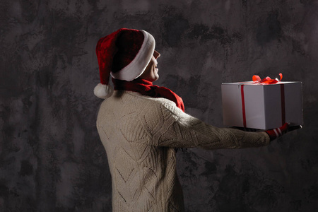 圣诞礼物概念。 戴圣诞帽的人给你带礼物。 有魅力的男人拿着盒子。 圣诞节和新年假期庆祝活动。 男士戴帽子戴红围巾毛衣