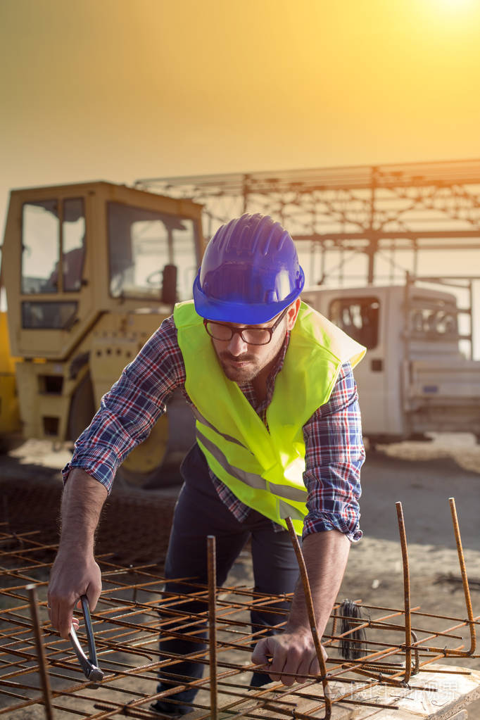 年轻有吸引力的建筑工人,戴着头盔,在建筑工地上工作加固网