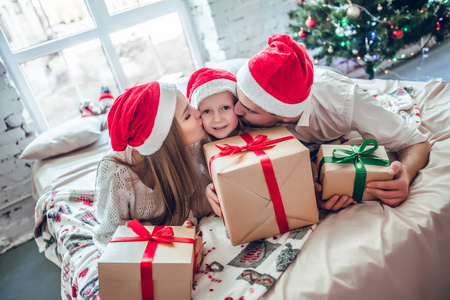在圣诞节的内部美丽的家庭。快乐的父母亲吻女儿，送圣诞礼物。