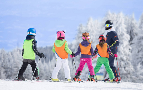 一群孩子和老师一起学习如何在斜坡上滑雪。蓝色的天空和白色的羽毛